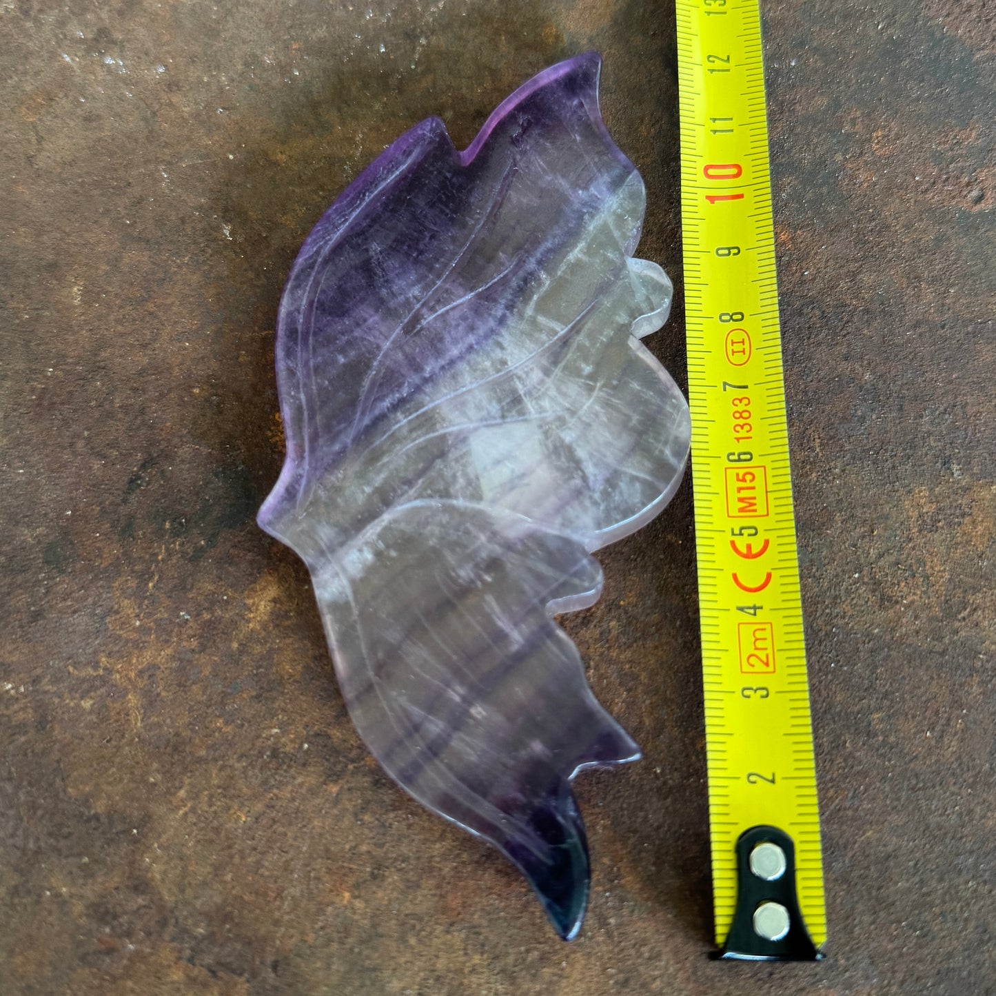 small_fluorite_crystal_wing next to a yellow measuring tape on a brown surface