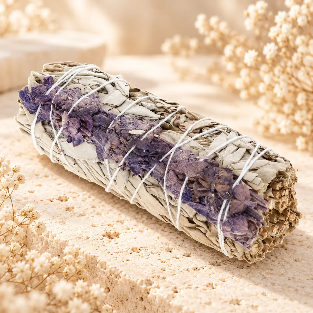 White Sage and Lavender Smudge Stick 13cm with dried purple lavender flowers tied to a white sage bundle on cream stone