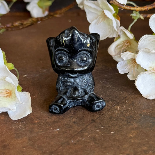 Black Obsidian Groot crystal carving seated on a wooden surface surrounded by white flowers