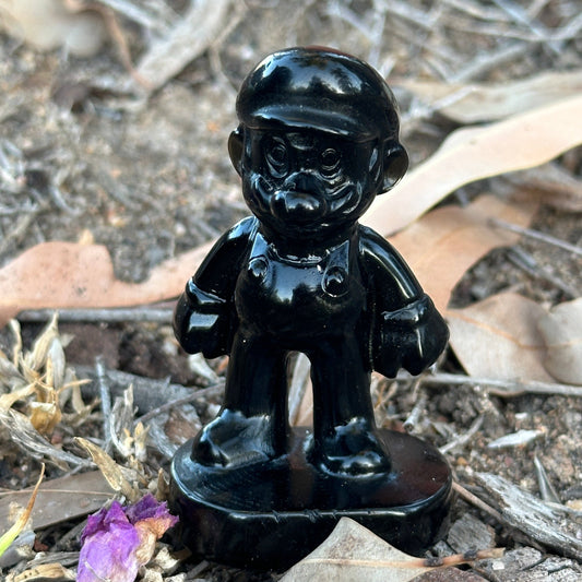 Black Obsidian Mario-inspired crystal carving standing outdoors among dry leaves and earth