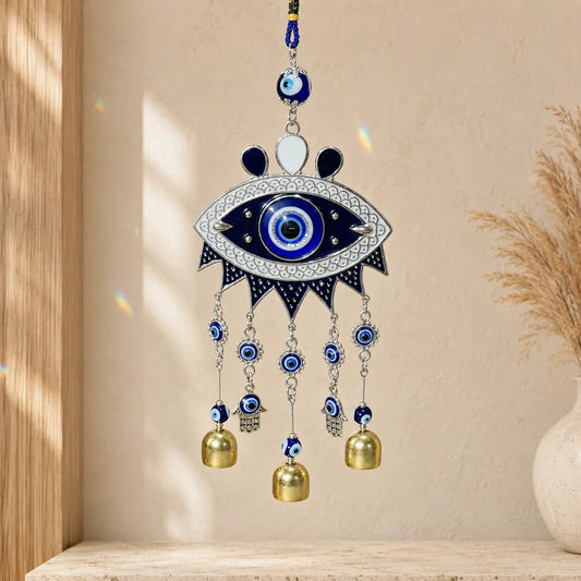 Blue Evil Eye Wind Chime/Suncatcher with two Hamsa hand charms and three gold-tone bells hanging against a warm cream wall