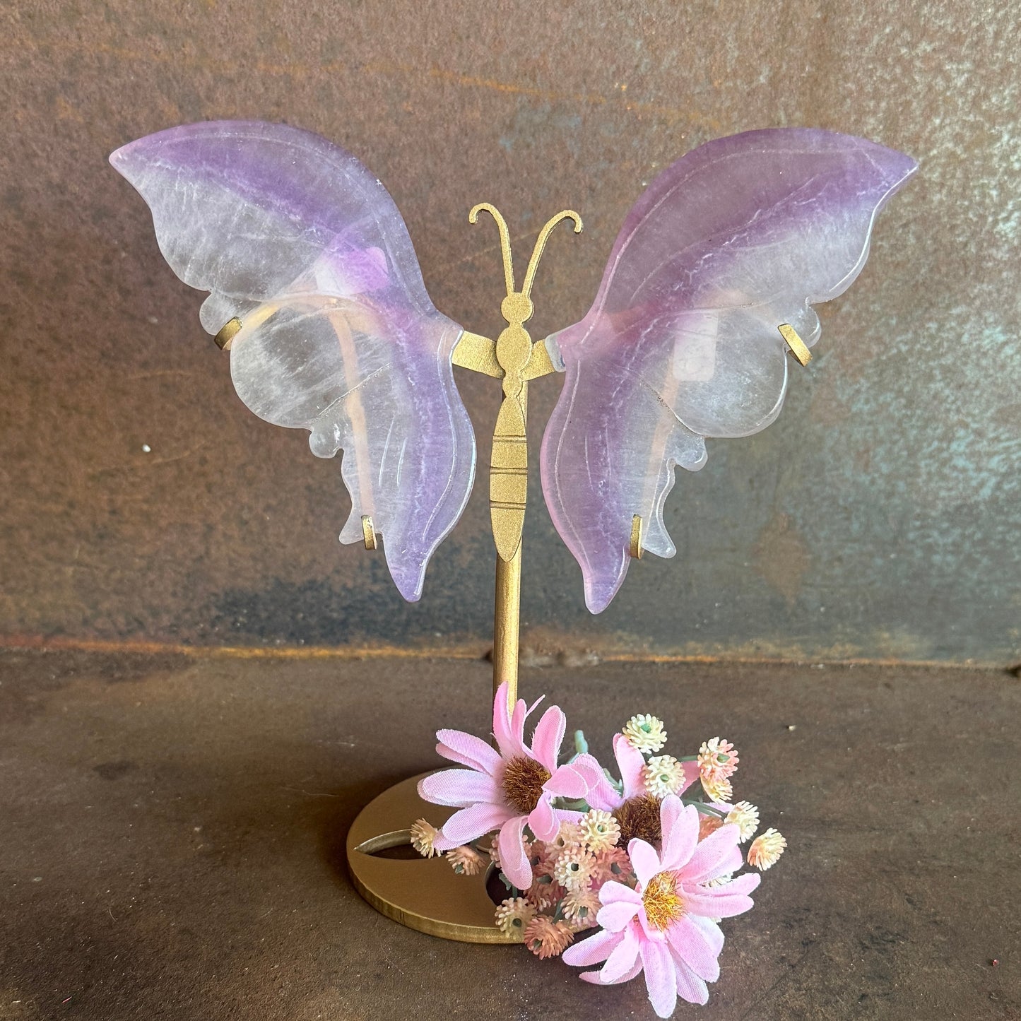 Decorative butterfly with purple wings and gold body on a stand with pink flowers against a brown background