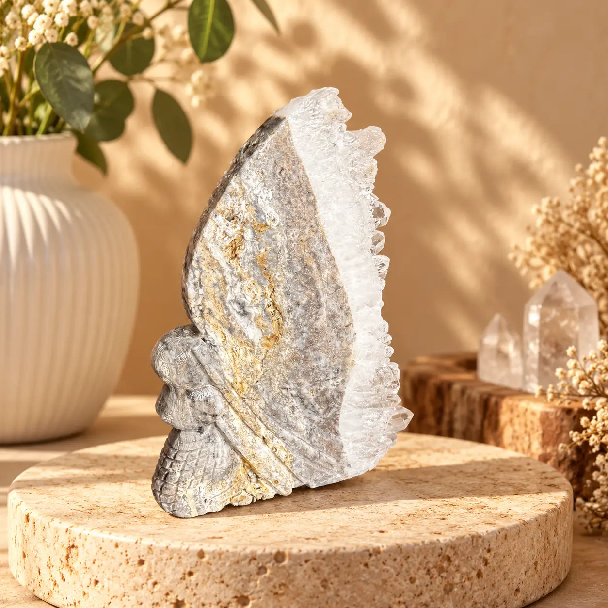 Mermaid quartz geode carving 167g with banded silver-grey body, carved scale detail and raw white crystal cluster edge, styled on a travertine plinth