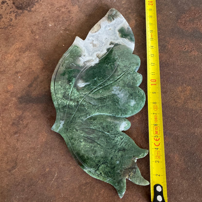 Moss Agate Crystal Wing with a measuring tape for scale on a brown surface