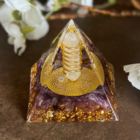 An Orgonite Pyramid featuring Amethyst and a Clear Quartz Crystal Double Point, with a gold-colored patterned base.