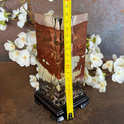 Picture Jasper crystal on timber stand for grounding energy, calm, emotional balance and spiritual décor statement piece.a measuring tape for scale, set against a floral background.