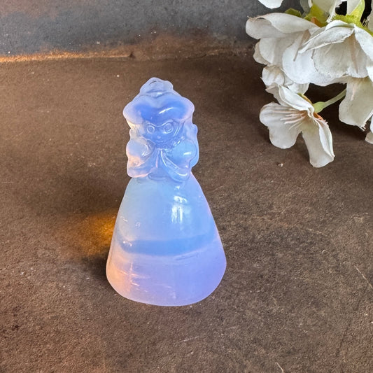 Pink Opalite Princess Peach-inspired crystal carving on a dark stone surface beside