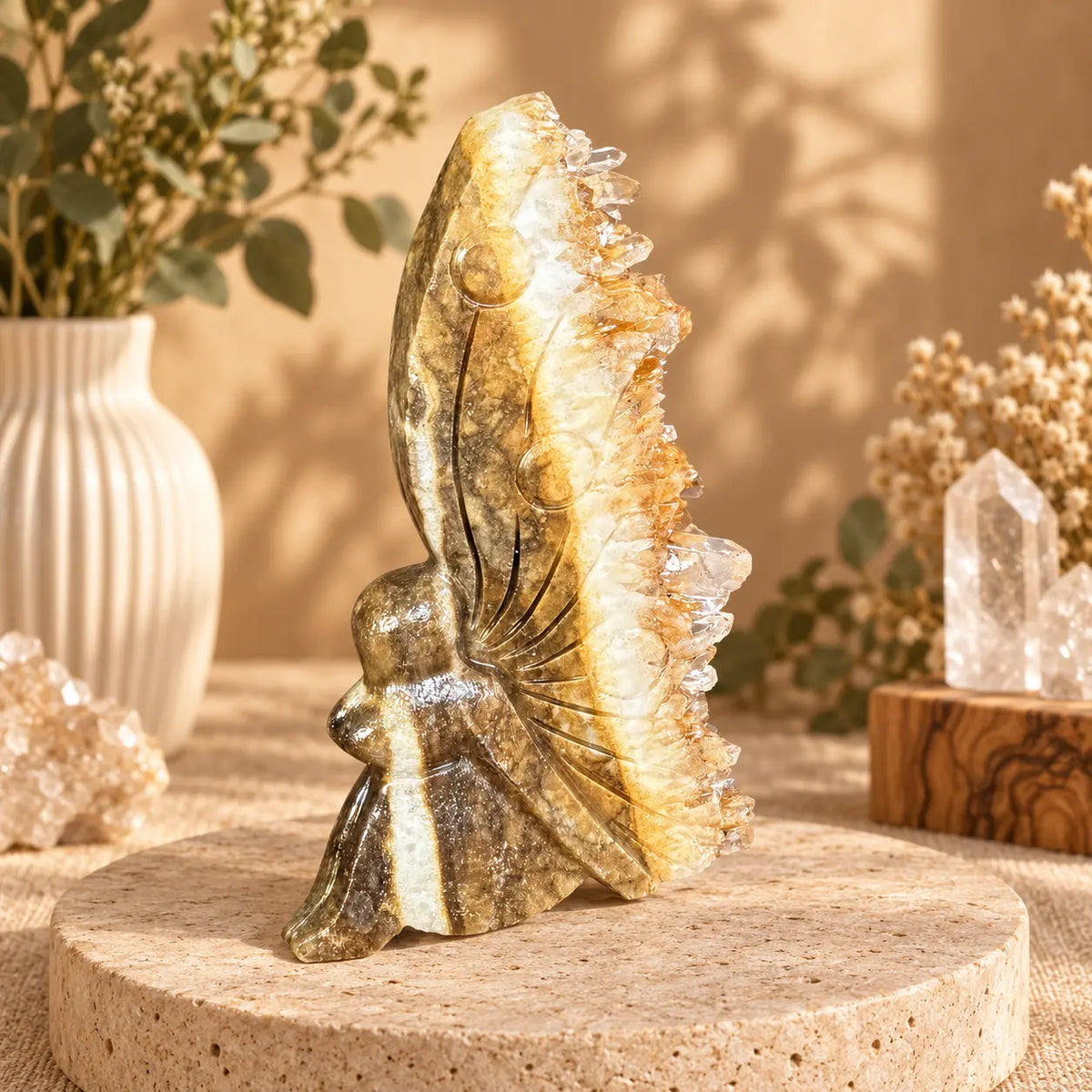 Quartz geode fairy carving 116g with warm golden-tan body, carved wing detail and dense raw crystal cluster edge, styled on a travertine plinth