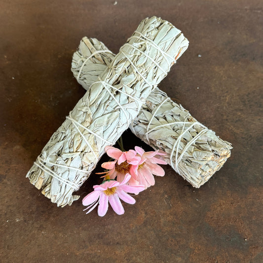 Two bundles of sage wrapped in twine with pink flowers on a dark surface