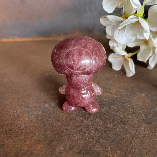 Toad-inspired crystal carving on a dark stone surface beside white flowers