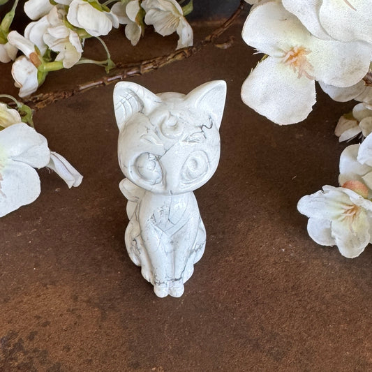 White Howlite Sailor Moon-inspired cat crystal carving with grey veining, large anime-style eyes and crescent moon detail, displayed with white flowers