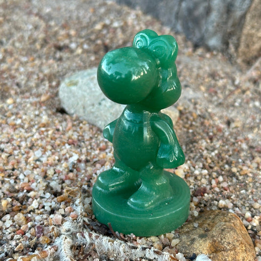 Green Aventurine Yoshi-inspired crystal carving standing on sandy ground with rocks
