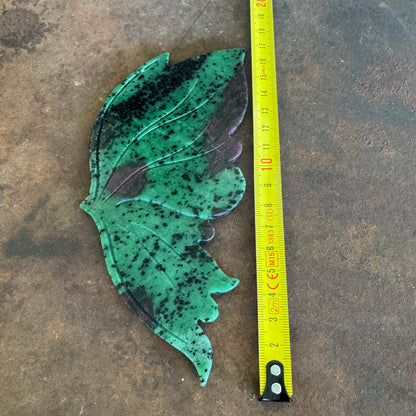 ruby in zoisite crystal wing next to a yellow measuring tape on a brown surface